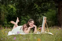 Jacksonville, FL portrait session capturing Palatka, senior of a creative young woman relaxing barefoot in a meadow, her easel nearby as she paints among soft summer blooms.