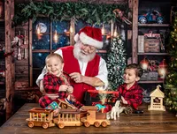 Child laughing with Santa while exploring handmade toys during a Santa's Workshop photography session in Jacksonville, Florida with Nature's Child Photography, surrounded by festive North Pole workshop details, glowing holiday magic, and matching Christmas pajamas.
