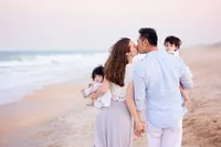 Ponte Vedra portrait session capturing A couple walking hand in hand along Ponte Vedra Beach, pausing for a kiss while holding their twin babies, both little ones glancing back toward the camera as waves roll in behind them during a Nature's Child Photography family portrait session.