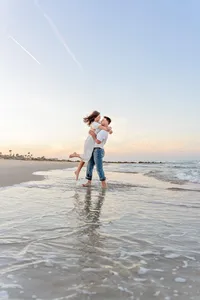 Professional photography by Nature's Child Photography: In Palm Coast, an engaged couple laughs as he spins her barefoot in the water during a beach engagement, their reflection rippling beneath them.