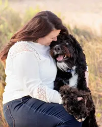 Ponte Vedra portrait session capturing Beach dog featuring a woman sitting with her fluffy black and white bernedoodle, their faces close as they look into each other’s eyes in warm evening light.