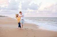 Ponte Vedra portrait session capturing Beach, a husband pulls his wife playfully close while they run through the sand, their footprints trailing behind them along the ocean.