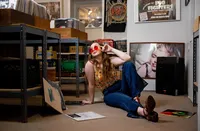 Professional photography by Nature's Child Photography: Photo of a young graduating senior in flared jeans and red sunglasses sitting among vintage records, styled with a nostalgic, music-inspired aesthetic.