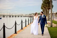 St. Augustine wedding capturing newlyweds strolling along the bayfront, palm trees lining the path and the Bridge of Lions rising in the distance. - A portrait experience by Nature's Child Photography.