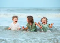 Three young siblings laughing and splashing in the shallow ocean waves during a beach child portrait session. (Photographed by Nature's Child Photography)