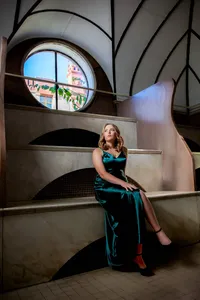 Jacksonville, FL portrait session capturing In St. Augustine, a high school senior in a rich emerald gown sits gracefully along sweeping stone curves, framed by historic arches and warm window light.