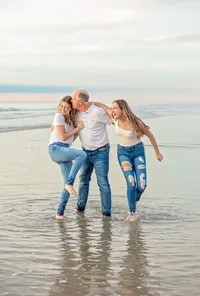 Jacksonville, FL portrait session capturing A father and his two teenage daughters as they walk barefoot in the ocean at sunrise on Micklers Beach, laughing and leaning into each other during a family portrait session with Nature's Child Photography.