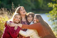 Edwardsville, Illinois family of a mother wrapped in a group hug with her three daughters, all smiling and holding each other close in golden light. (Photographed by Nature's Child Photography)