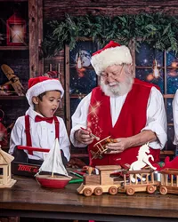 Child watching in amazement as Santa creates a magical wooden toy during a Santa’s Workshop photography session in Jacksonville, Florida with Nature’s Child Photography, surrounded by handmade toys, glowing workshop lights, and cozy North Pole details.