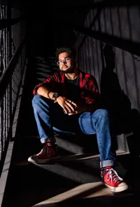High school senior in O’Fallon, Illinois seated on metal stair steps with striking directional light and deep shadows, creating a dramatic editorial senior portrait. - A portrait experience by Nature's Child Photography.