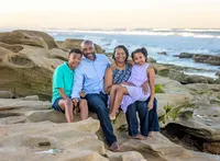 Palm Coast, family capturing a mother and father sitting on seaside rocks with their two school-aged children, the ocean stretching out behind them in soft evening light. (Photographed by Nature's Child Photography)