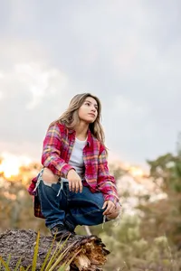 Professional photography by Nature's Child Photography: St. Johns, senior of a poised high school senior resting on a log at sunset, her flannel catching the last warm light of the day.