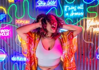 Professional photography by Nature's Child Photography: St. Augustine senior stands beneath glowing neon signs, curly hair framing her face as she throws her head back in bold, expressive energy during a vibrant urban senior portrait session.