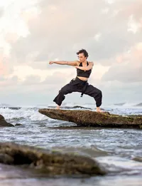 Professional photography by Nature's Child Photography: Graduating senior in Palm Coast, featuring a martial artist performing a powerful karate stance on a rocky shoreline at sunset.