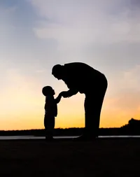 Professional photography by Nature's Child Photography: Along the Intracoastal Waterway in Palm Coast, a father bends toward his young son, their hands meeting in a tender sunset silhouette during a family portrait session..