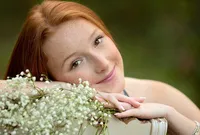 Jacksonville, FL portrait session capturing Close-up senior in St. Johns, of a freckled high school senior with red hair gently smiling beside a bouquet of white blooms.