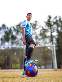 Professional photography by Nature's Child Photography: In St. Johns, a varsity soccer senior stands poised with his foot planted on a bold red and blue soccer ball, commanding the field with quiet intensity.