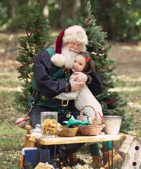 Young girl shares a warm hug with Santa during a Santa's Enchanted Forest photography session in St. Johns, Florida, surrounded by woodland Christmas trees, nature-inspired holiday details, and the magic of the season.