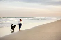 On Ponte Vedrra Beach, capturing a woman walking along the shoreline with her black doodle, both reflected in the wet sand as waves roll in. - A portrait experience by Nature's Child Photography.