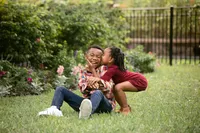 Sibling chaos in full force during a Jacksonville family photography session with Nature’s Child Photography as little sister launches a surprise cheek kiss and her brother completely loses it laughing in the grass.
