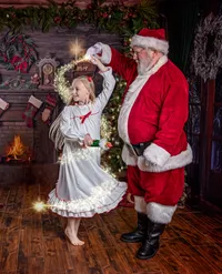 Young girl twirls with Santa beside a glowing fireplace during a Santa's Magical Christmas photography session in Jacksonville, Florida, surrounded by Christmas garlands, twinkling lights, and holiday wonder.