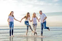 A family joins hands and playfully kicks water into the air at sunrise on Beach, their laughter carrying across the shoreline during a family portrait session. - A portrait experience by Nature's Child Photography.