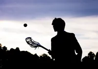 Jacksonville, FL portrait session capturing Silhouetted high school lacrosse player at sunset in St. Johns, holding his stick as the sky glows behind him in a dramatic senior sports session.