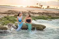 Mermaid-inspired image of two girls laughing together on a coastal rock while ocean waves splash at sunset in Palm Coast during a Mermaid Imagination Session. (Photographed by Nature's Child Photography)