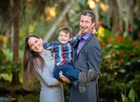 In Palm Coast, a mother and father hold their young son between them, all three laughing as he wraps his arms around his dad’s shoulders during a heartfelt family session. (Photographed by Nature's Child Photography)