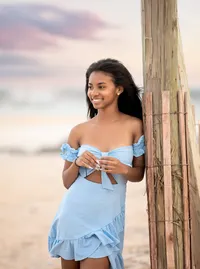 A Vilano Beach, senior captures a poised high school senior resting against rustic dune fencing, her serene expression and wind-swept hair glowing in pastel sunset tones. (Photographed by Nature's Child Photography)