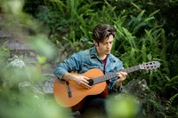 Jacksonville, FL portrait session capturing High school senior in Palatka, playing acoustic guitar among soft greenery, blending artistry and introspection in a nature-inspired senior photo session taken by Nature's Child Photography.