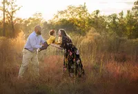 Jacksonville, FL portrait session capturing A joyful couple play with their toddler in a field of warm autumn grass in St. Johns, the father lifting her high as the mother leans in for a loving kiss during an outdoor family session with Nature's Child Photography.