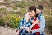 A joyful mother sits in the sand on Ponte Vedra Beach, as her two sons squeeze in close, laughing and embracing her during a candid coastal family portrait session. (Photographed by Nature's Child Photography)