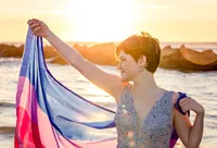 Vilano Beach, senior at sunrise, where a senior lifts a flowing Pride flag in pink, purple, and blue tones against the glowing ocean horizon. - A portrait experience by Nature's Child Photography.