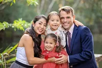Family capturing a mom and dad embracing their two little girls, their faces close and expressions bright with shared joy. - A portrait experience by Nature's Child Photography.