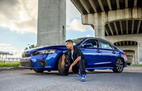 High school senior poses beside his blue car beneath an overpass, creating a poised, modern senior with bold urban energy. (Photographed by Nature's Child Photography)