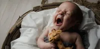 In St. Johns, a newborn lets out a wide, sleepy yawn while clutching a tiny stuffed giraffe, photographed during a cozy in-home lifestyle newborn. - A portrait experience by Nature's Child Photography.