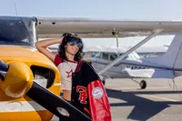 Professional photography by Nature's Child Photography: High school senior, poses beside a vintage-style airplane, varsity jacket draped over her shoulder, blending aviation edge with senior year confidence.