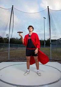 High school senior discus athlete stands in the throwing circle in St. Johns, holding his discus during a bold senior sports session. (Photographed by Nature's Child Photography)
