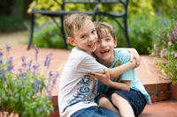Two energetic boys in Palm Coast, burst into laughter while hugging on a brick patio during a carefree outdoor portrait session. - A portrait experience by Nature's Child Photography.