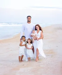On Ponte Vedra Beach, a mother and father stand barefoot in the sand holding their baby while their two daughters stand close at their sides during a beach family portrait session. (Photographed by Nature's Child Photography)
