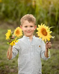 Young boy smiling with dirt on his hands from picking sunflowers during a child portrait session in a sunflower field in Callahan. - A portrait experience by Nature's Child Photography.