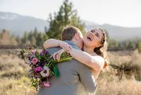 Bride laughing while embracing her groom during a mountain wedding photography session in Graeagle, California with Nature’s Child Photography, colorful bouquet and warm golden light surrounding the couple against a Sierra mountain backdrop.