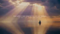Psalm 28:7 Bible verse displayed over golden rays of light breaking through clouds above calm water, symbolizing trust in God as strength and shield