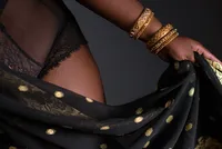 Close detail of a hand gathering black and gold sari fabric against skin, stacked gold bangles at the wrist.