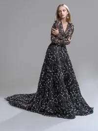 Model in a black gown with sheer sleeves and a celestial pattern, full train spread across a grey studio floor.
