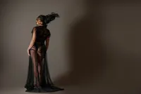 Dancer in a sheer black gown arching backward with her hair in motion against a warm brown backdrop.
