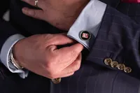 Close detail of a man adjusting his cufflink on a navy pinstripe suit sleeve, wristwatch visible.