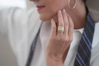 Close detail of a woman's hand resting near her chin, a large ring in focus against a white shirt and striped tie.