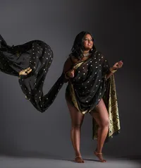 A woman draped in a flowing black and gold sari stands barefoot against a dark background. Her arm is raised, making the fabric billow dramatically—an image perfect for fashion-inspired editorial portraits Washington DC.
